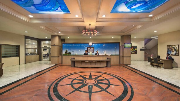Un vestíbulo de hotel con una recepción central, un diseño de brújula grande en el suelo y un techo con patrones de olas azules.