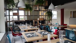 Een modern restaurantinterieur met meerdere eettafels, stoelen en hangplanten.