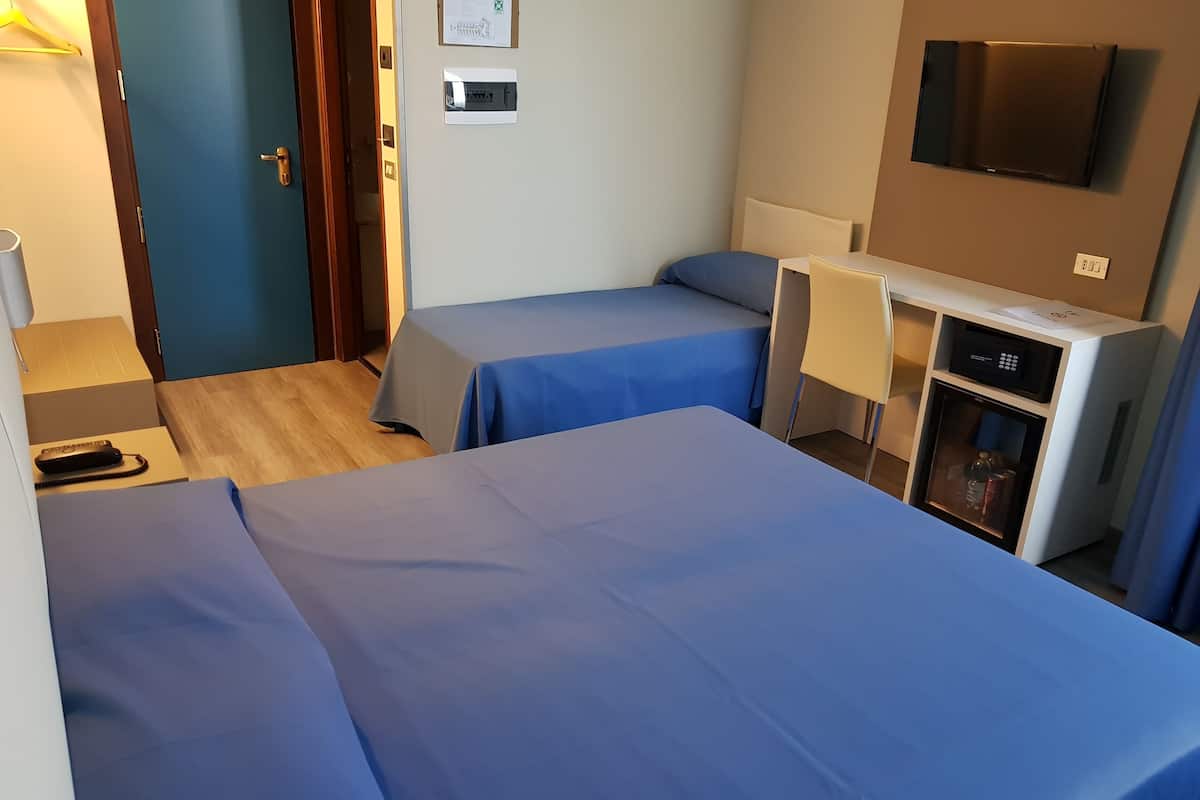 A hotel room with two single beds, a desk with a chair, a minibar, and a television mounted on the wall.