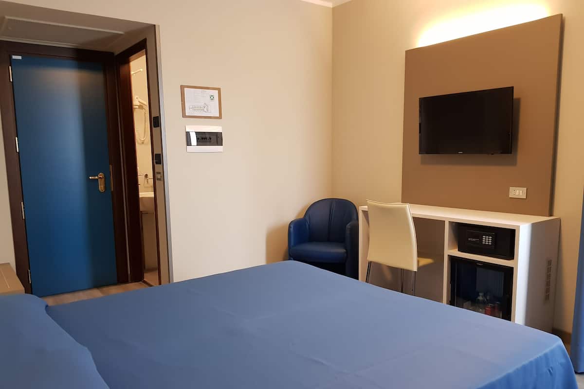 A hotel room with a bed, a desk with a chair, a television, and a small kitchenette.