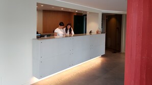 Een receptiegedeelte met een modern ontwerp, met een receptiebalie, een glazen vitrine met objecten, en een wand van houten panelen.