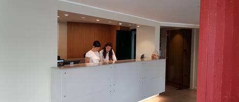 Zona de recepción con diseño moderno, que incluye un mostrador de recepción, una vitrina con objetos y un panel de pared de madera.
