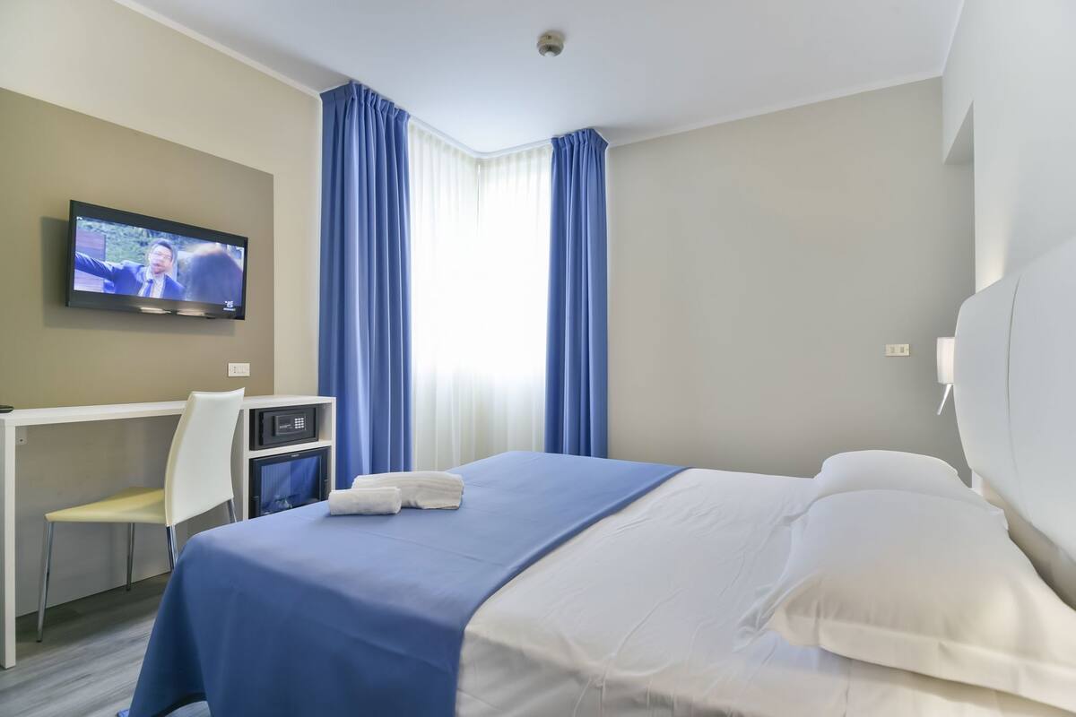 A hotel room with a bed, a desk, a chair, a television, and curtains.