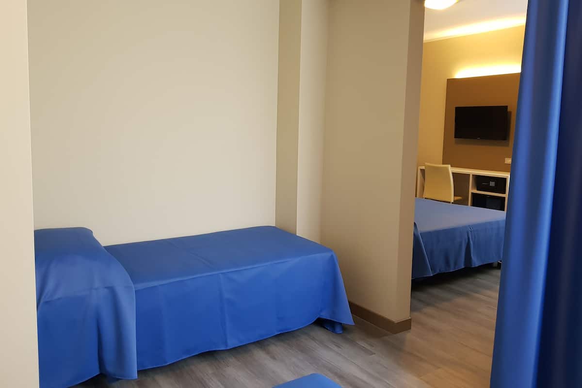 A hotel room with two single beds, a flat-screen TV mounted on the wall, and a wooden floor.