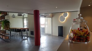 Een moderne kantoorruimte met een grote glazen pot vol snoep op een toonbank, een houten tafel met stoelen en een rode pilaar.