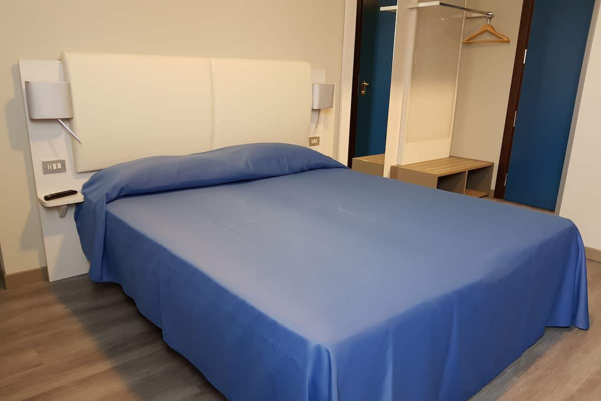 A neatly made bed with a blue bedspread, a bedside table with a lamp, and a mirror on the wall.