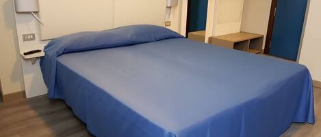 A neatly made bed with a blue bedspread, a bedside table with a lamp, and a mirror on the wall.