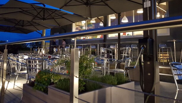 Een terras met meerdere tafels en stoelen, parasols en een modern architectonisch ontwerp.
