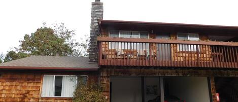 A two-story building with a wooden facade, a balcony with a railing, and a car parked in a garage.