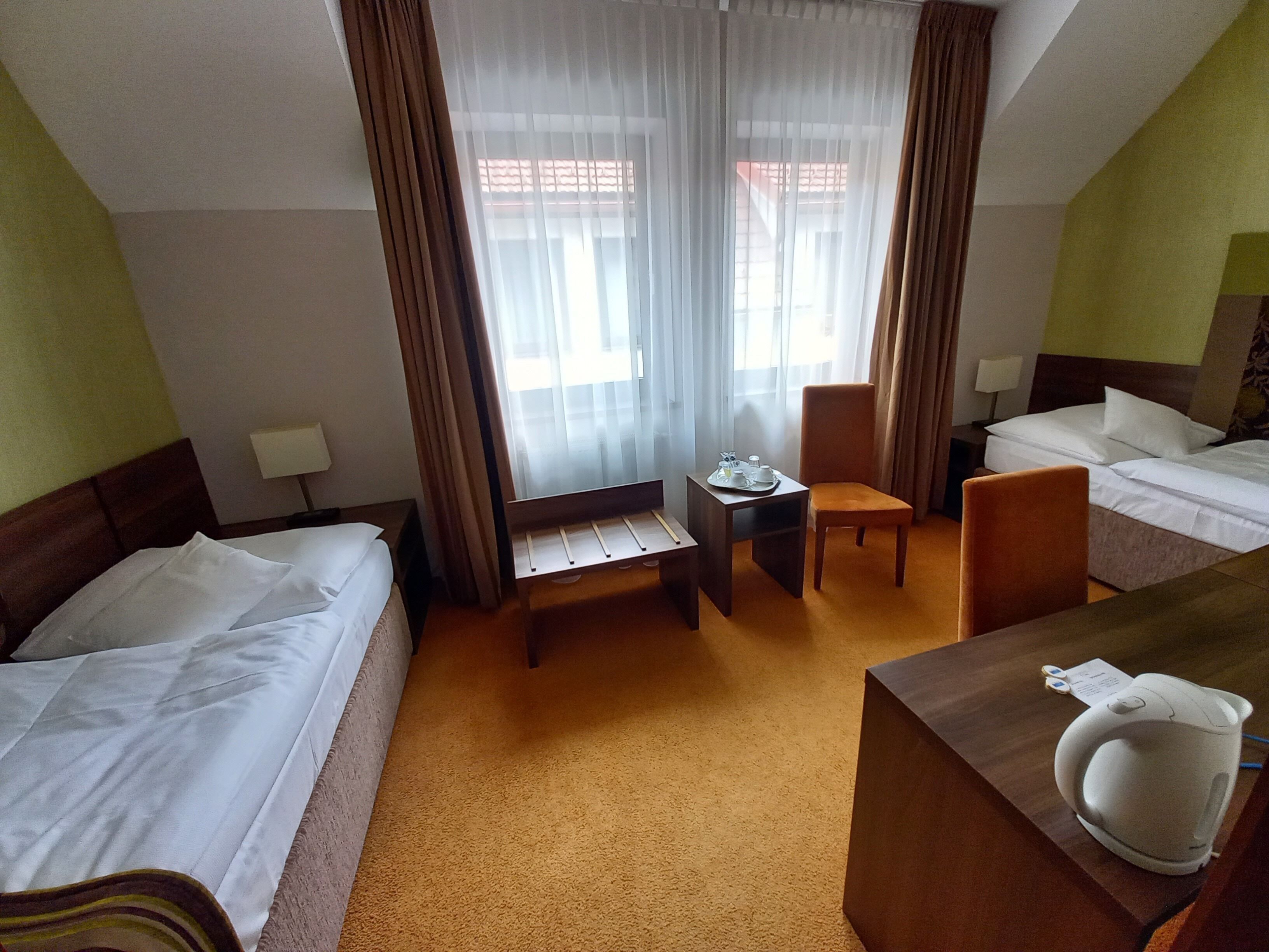 A hotel room with two beds, a small table with a tray, a chair, and a kettle on a wooden table.