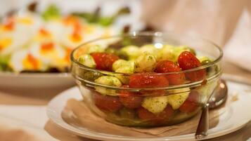 A glass bowl of salad with tomatoes and green leaves on a plate.
