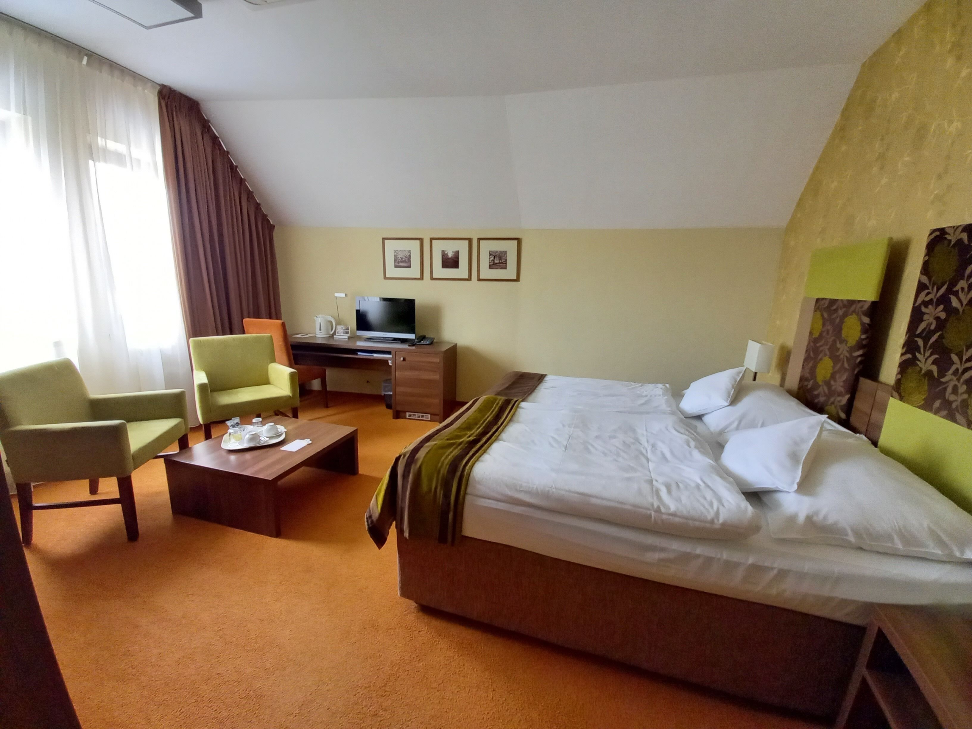 A hotel room with a bed, two chairs, a desk with a computer, a coffee table, and a TV.