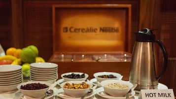 A breakfast buffet with various cereals, fruits, and a hot milk station.
