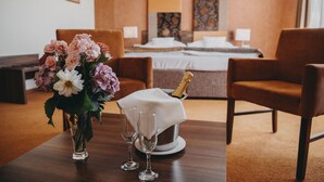 Ein Hotelzimmer mit einem Bett, zwei Stühlen, einem Tisch mit Blumenvase, zwei Gläsern und einer Champagnerflasche.