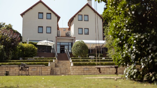 A two-story building with a symmetrical facade, a central entrance with steps, and a small garden area with neatly trimmed hedges and a single tree.