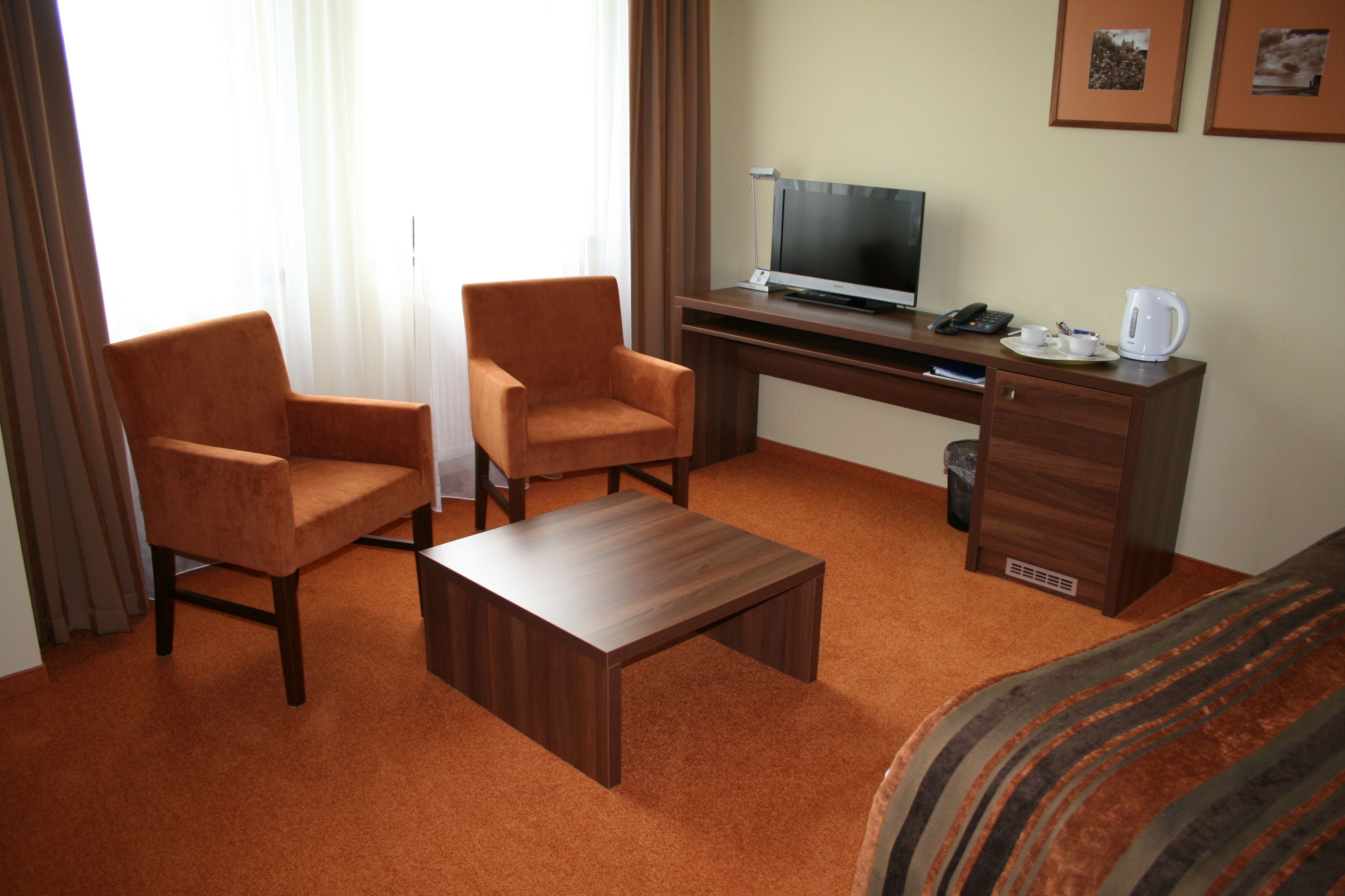 A hotel room with a wooden desk, two armchairs, a coffee table, and a bed with striped bedding.