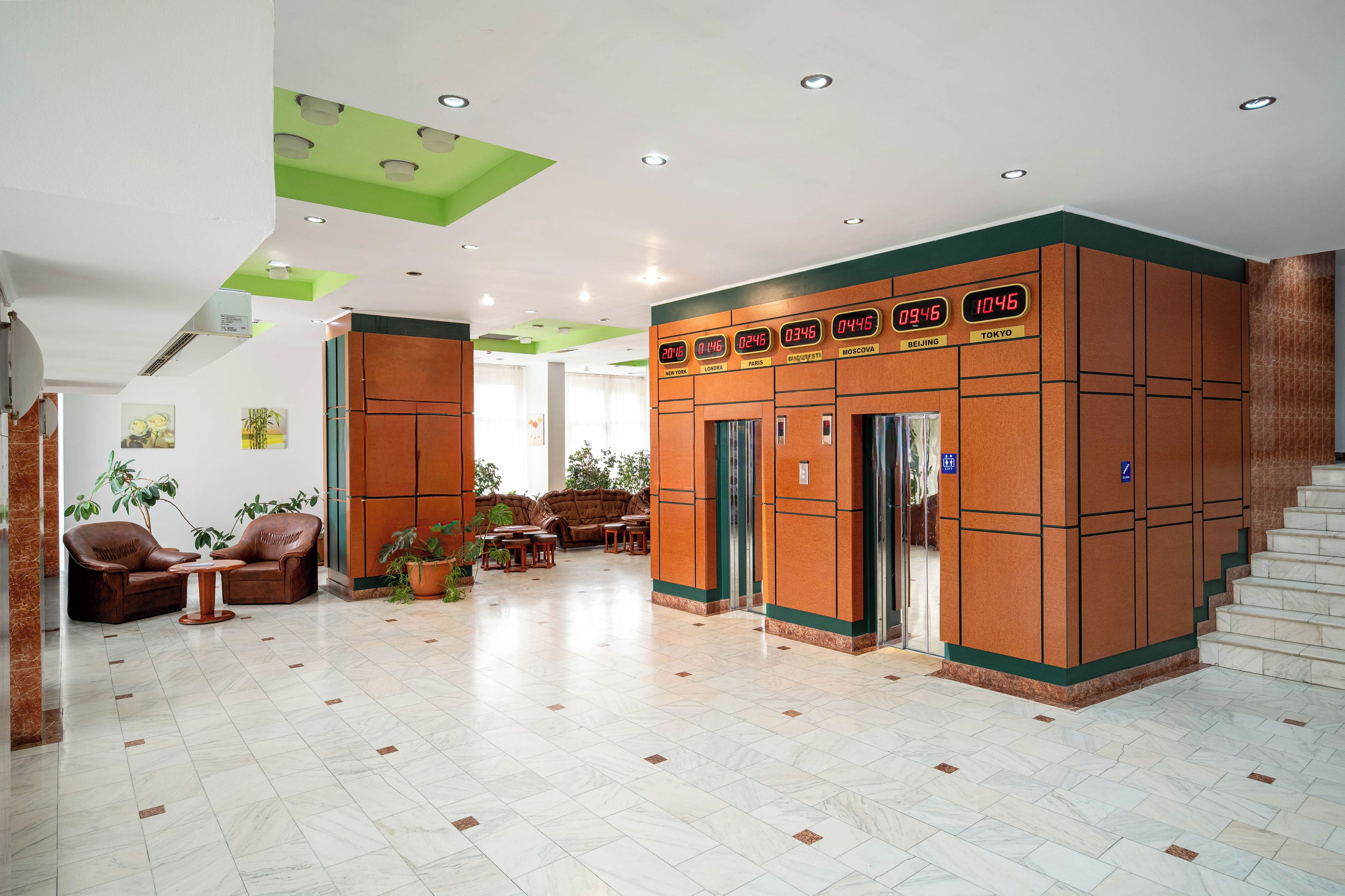 A lobby with a seating area, a staircase, and a wall with a digital clock displaying times in various cities.