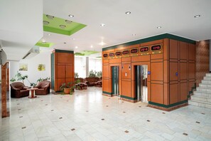 A lobby with a seating area, a staircase, and a wall with a digital clock displaying times in various cities. - Egreta (Tulcea)