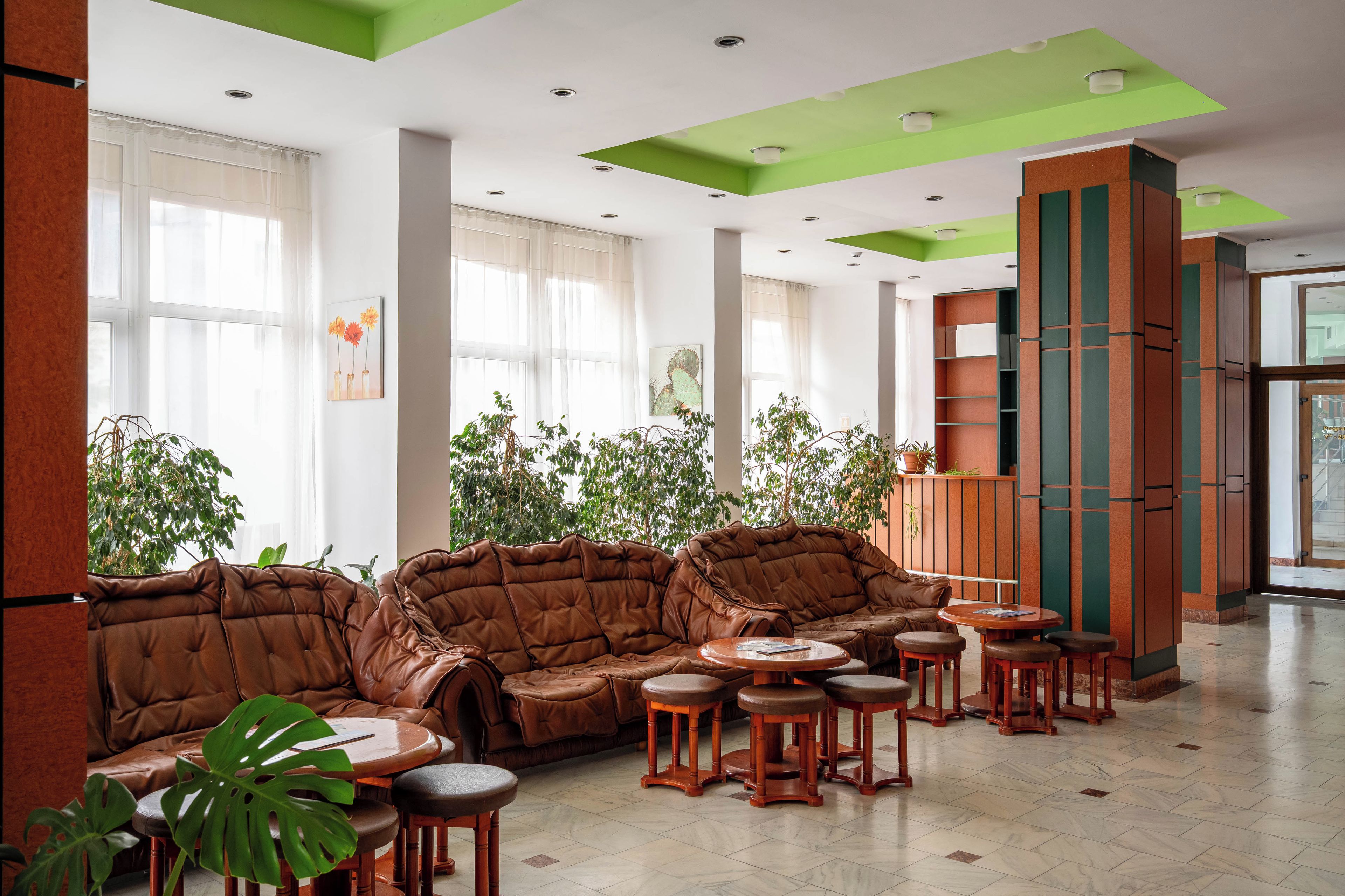 A spacious lobby with leather sofas, wooden stools, and a large potted plant.