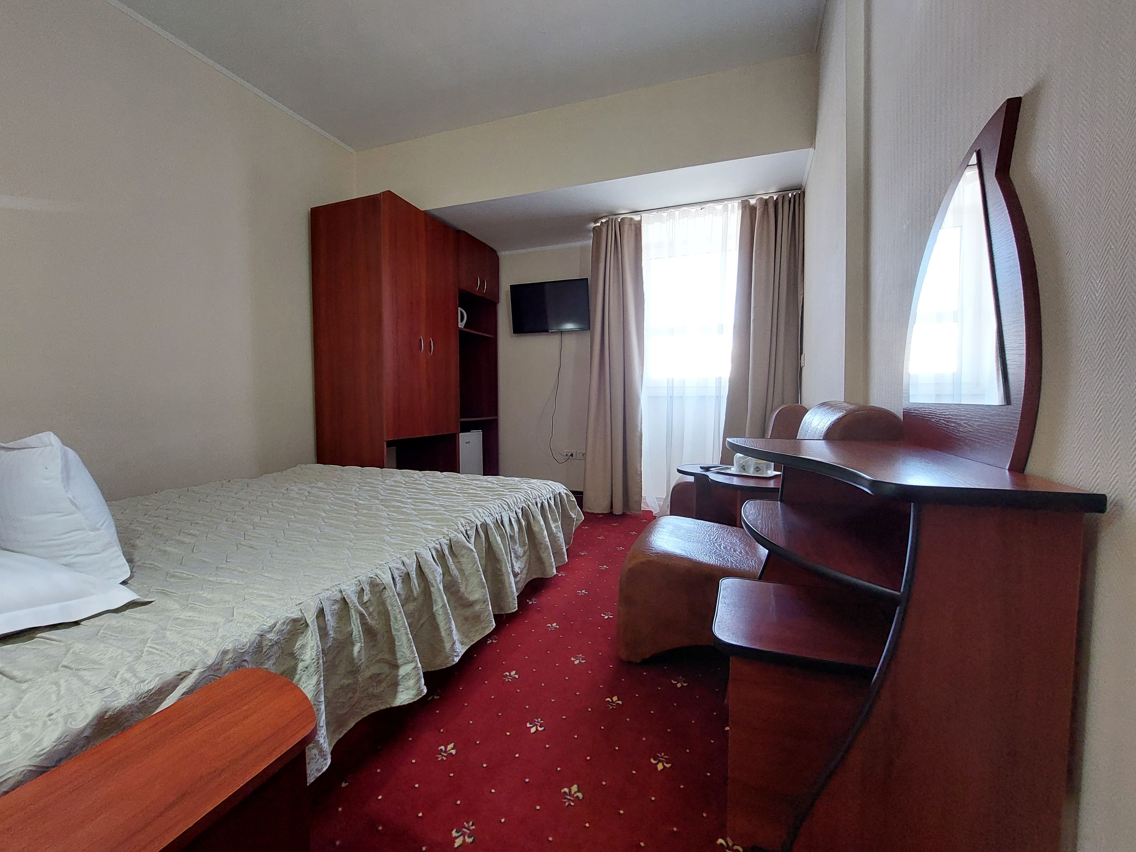 Une chambre d’hôtel équipée d’un lit, d’un bureau, d’une armoire, d’une télévision et d’une fenêtre avec des rideaux.