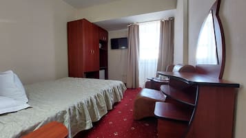 Une chambre d’hôtel équipée d’un lit, d’un bureau, d’une armoire, d’une télévision et d’une fenêtre avec des rideaux.