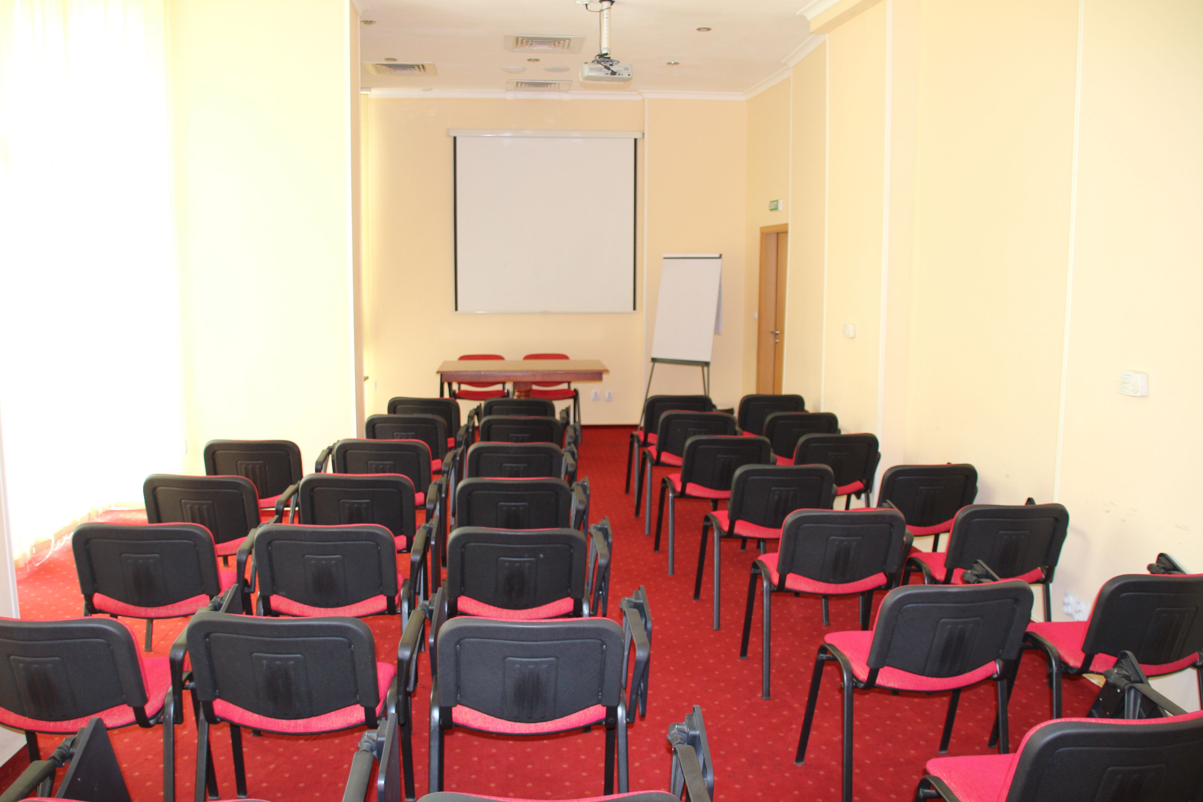 Un salón de conferencias con filas de sillas, una pizarra y una pantalla de proyector.