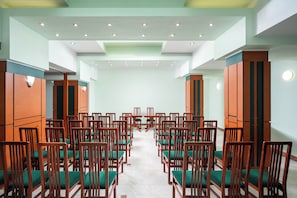 Un salón de conferencias con filas de sillas y mesas de madera, suelo de baldosas e iluminación empotrada en el techo.