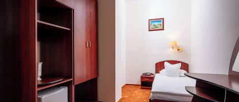 Habitación de hotel con cama, escritorio, armario, mesita de noche y lámpara de pared.