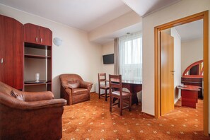 A room with a wooden cabinet, leather armchair, dining table with chairs, and a television on the wall.