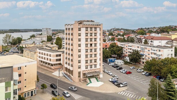A hotel with a prominent corner location, a parking lot with multiple cars, and a view of the surrounding cityscape. - Egreta (Tulcea)