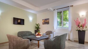 Un salon moderne doté d’un téléviseur à écran plat, de deux canapés gris, d’une table basse agrémentée d’un arrangement floral et d’une grande fenêtre avec des rideaux.