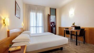 Una camera d'albergo con un letto, comodini, una scrivania con una sedia, un portatile e una piccola pianta in vaso.