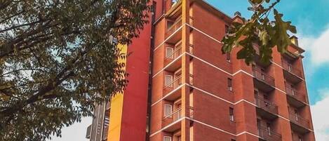 A multi-story building with a red facade, balconies, and a clear sky.