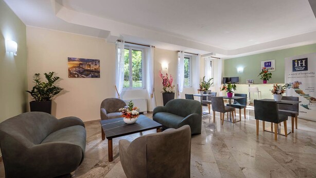 Un hall d’hôtel comprenant des espaces aménagés avec des sièges, un comptoir d’accueil et une grande fenêtre avec des rideaux.