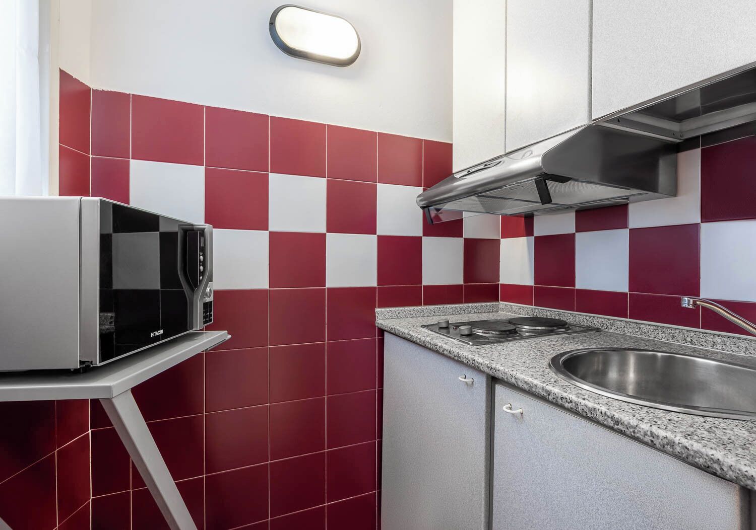 Une cuisine avec des carreaux rouges et blancs, un four à micro-ondes, une cuisinière et un évier en acier inoxydable.