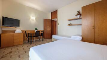 Una habitación de hotel con cama, escritorio y silla, televisión, armario y estante con una planta.
