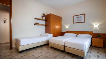 Habitación de hotel con cama doble, cama individual, armario de madera, mesitas de noche y un cuadro enmarcado en la pared.