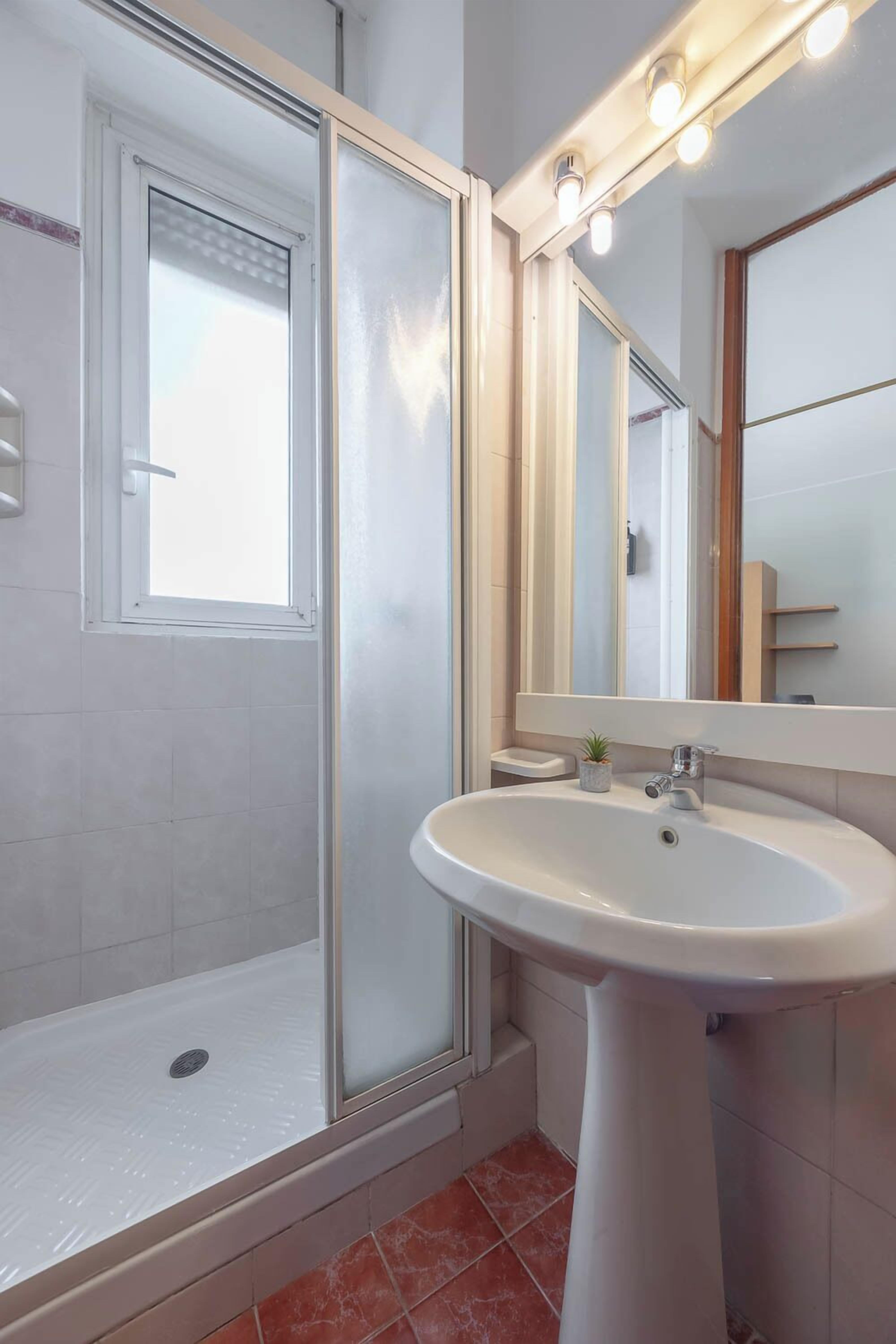 Une salle de bain moderne avec une douche à parois de verre, un lavabo sur colonne et un grand miroir avec éclairage intégré.