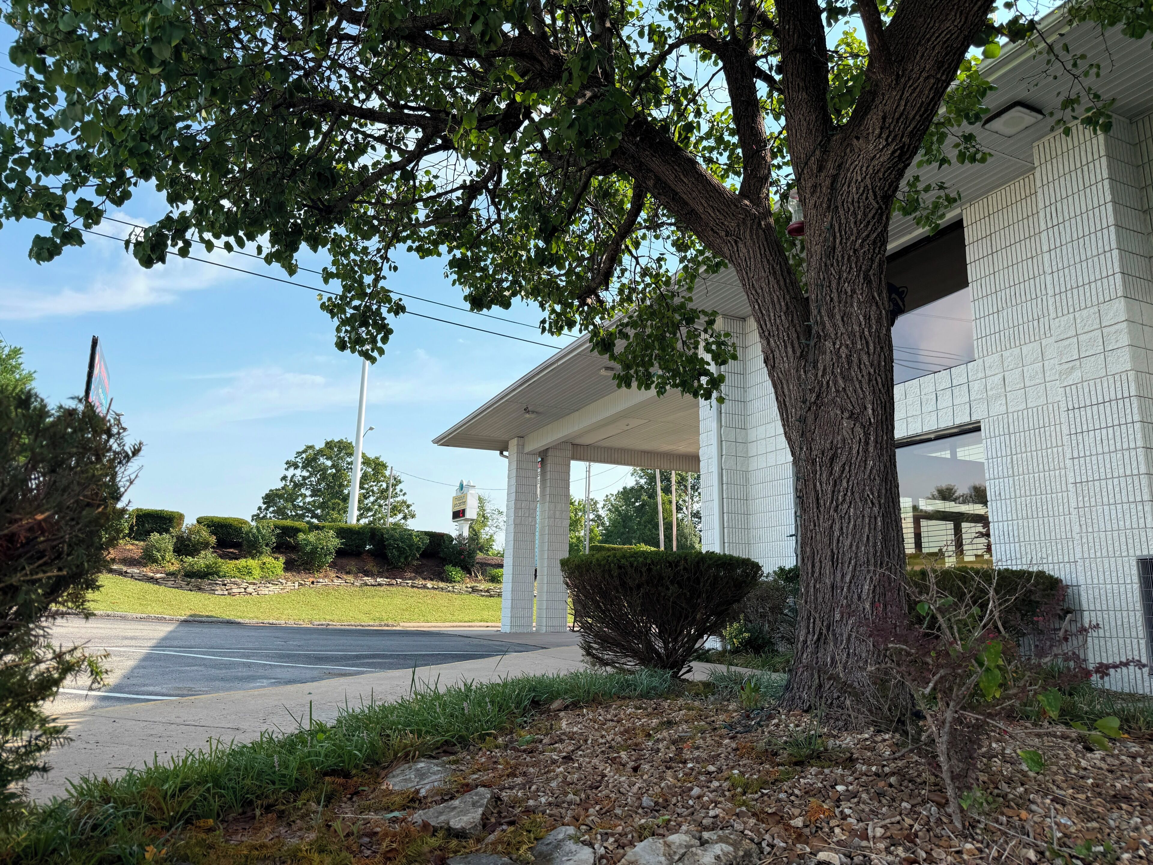 A two-story building with a covered porch, a large tree in front, and a clear sky.