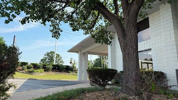 A two-story building with a covered porch, a large tree in front, and a clear sky.