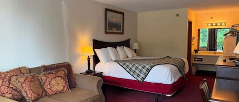 A hotel room with a bed, a sofa, a table, and a desk with a mirror.