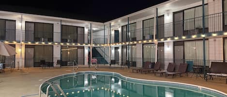 A hotel with a swimming pool, outdoor seating, and a covered area with string lights.