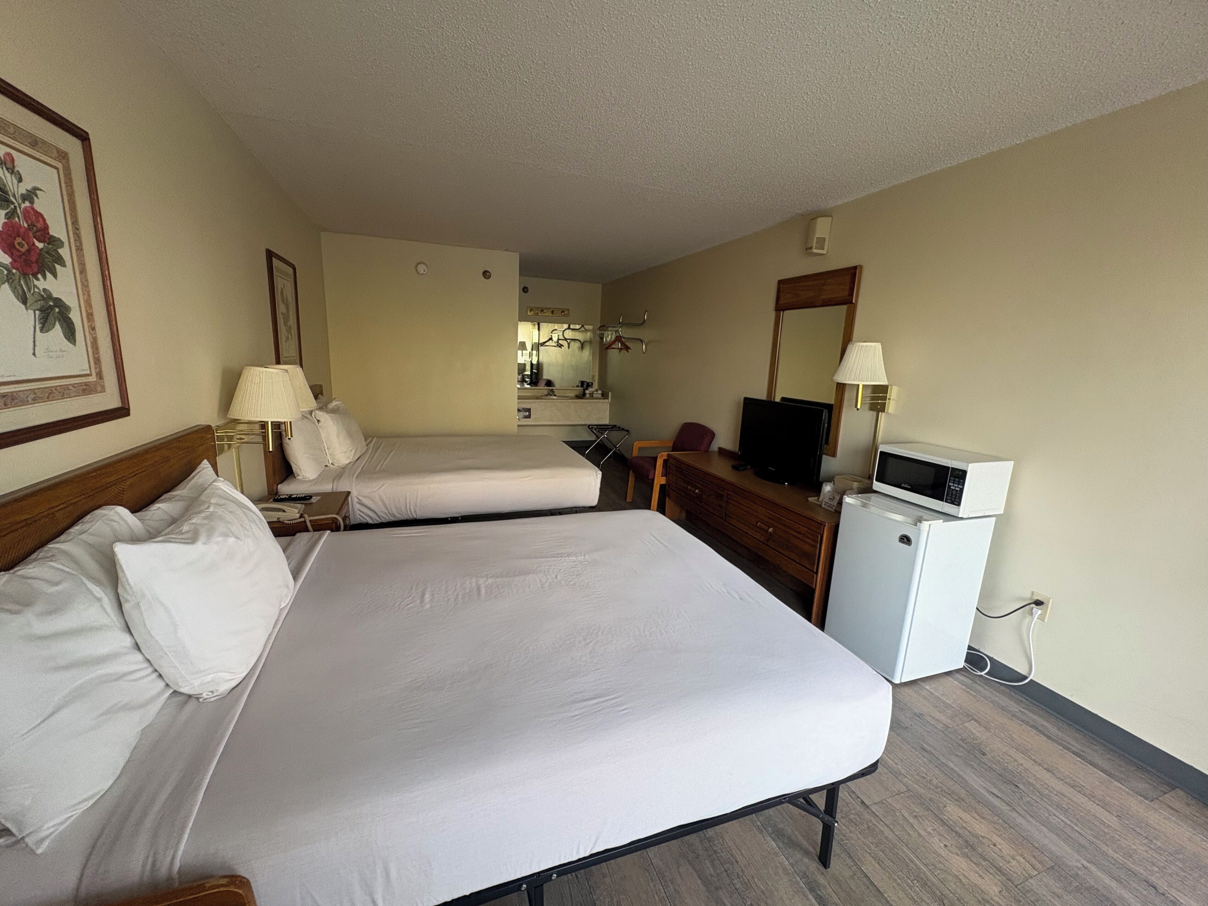 Una habitación de hotel con dos camas, un escritorio, un televisor, un microondas y un refrigerador pequeño.