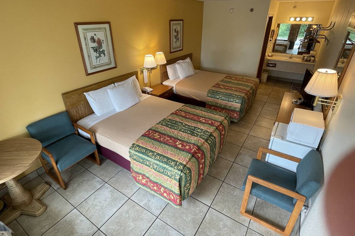 Habitación de hotel con dos camas, una mesita, una silla, un espejo y ventana con vistas.