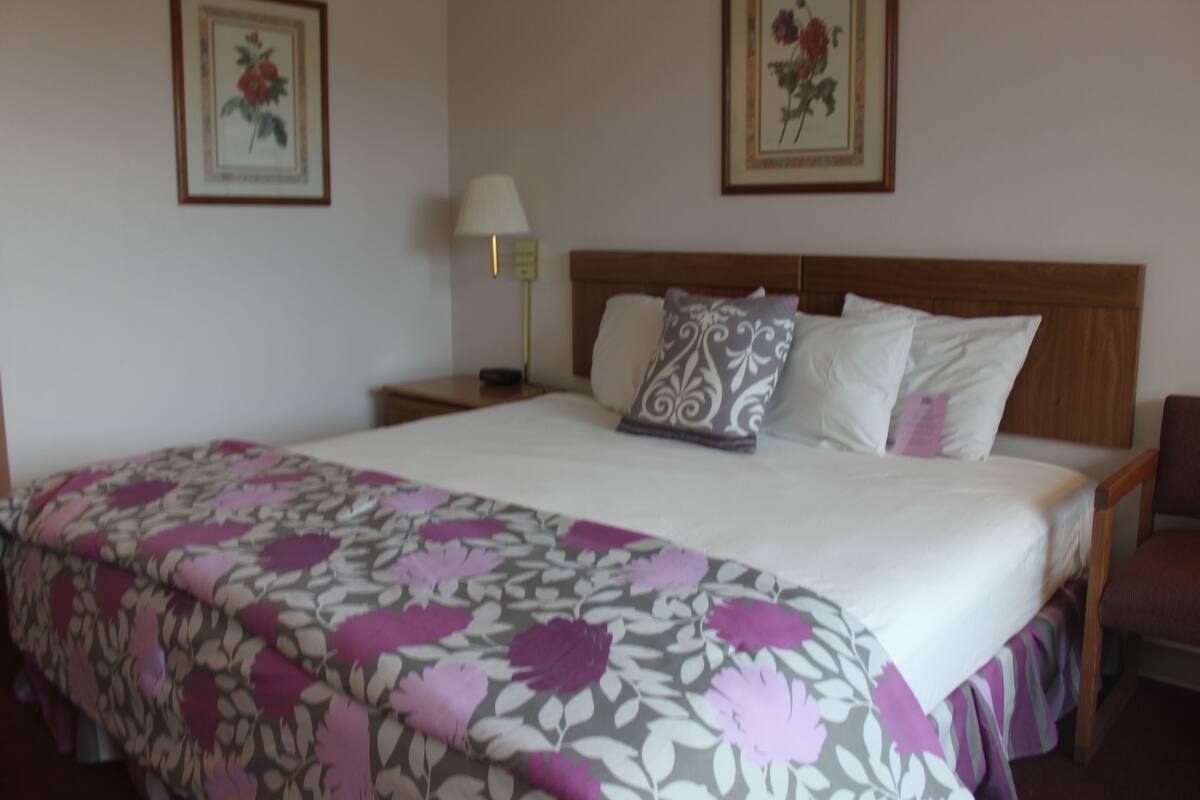 Una cama bien hecha con un edredón estampado con motivos florales, un cabecero de madera y dos cuadros con flores en la pared.