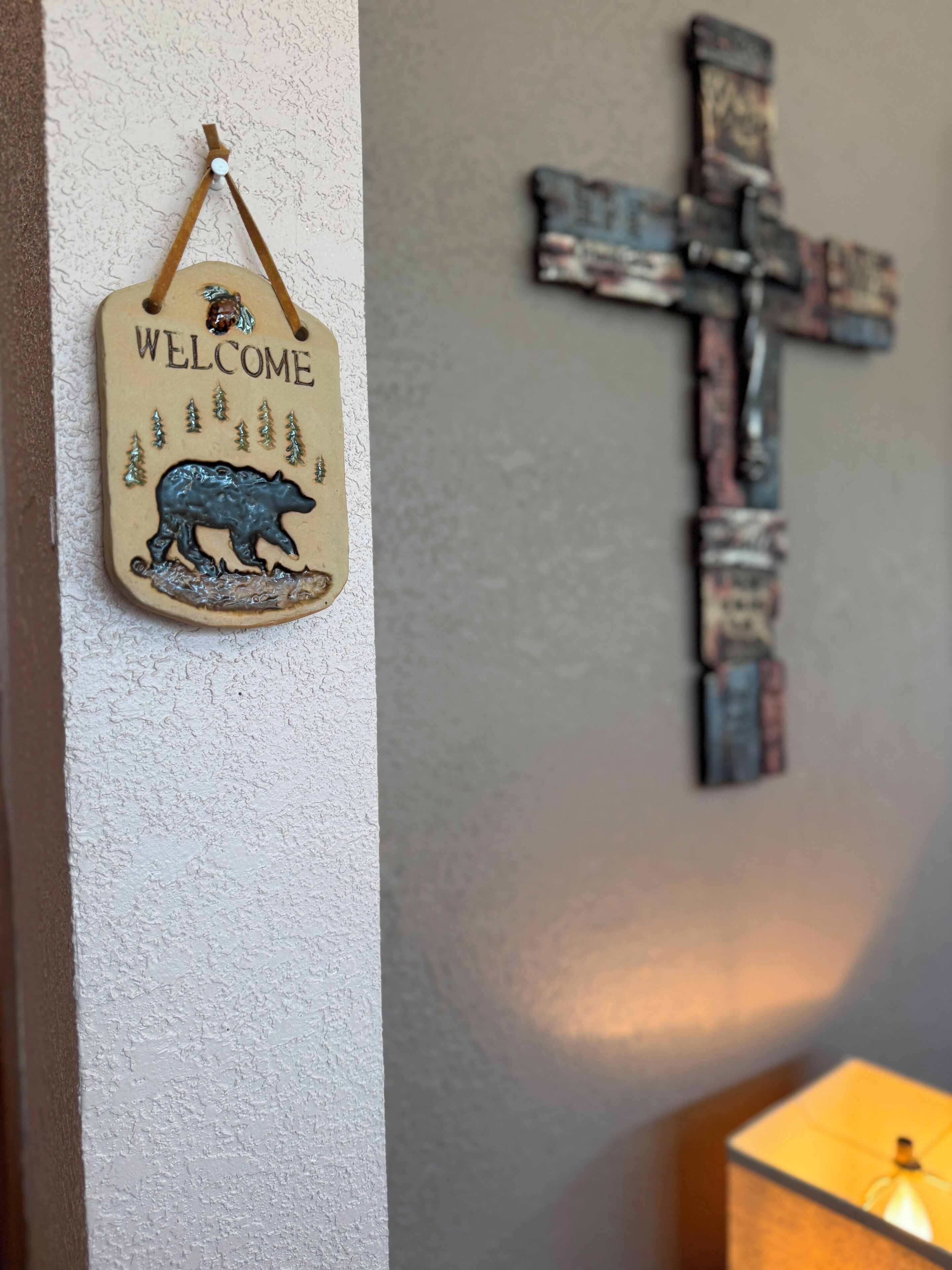 A welcome sign with a bear and trees, a rustic cross, and a lamp.