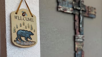 A welcome sign with a bear and trees, a rustic cross, and a lamp.