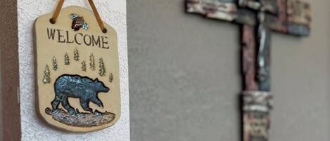 A welcome sign with a bear and trees, a rustic cross, and a lamp.