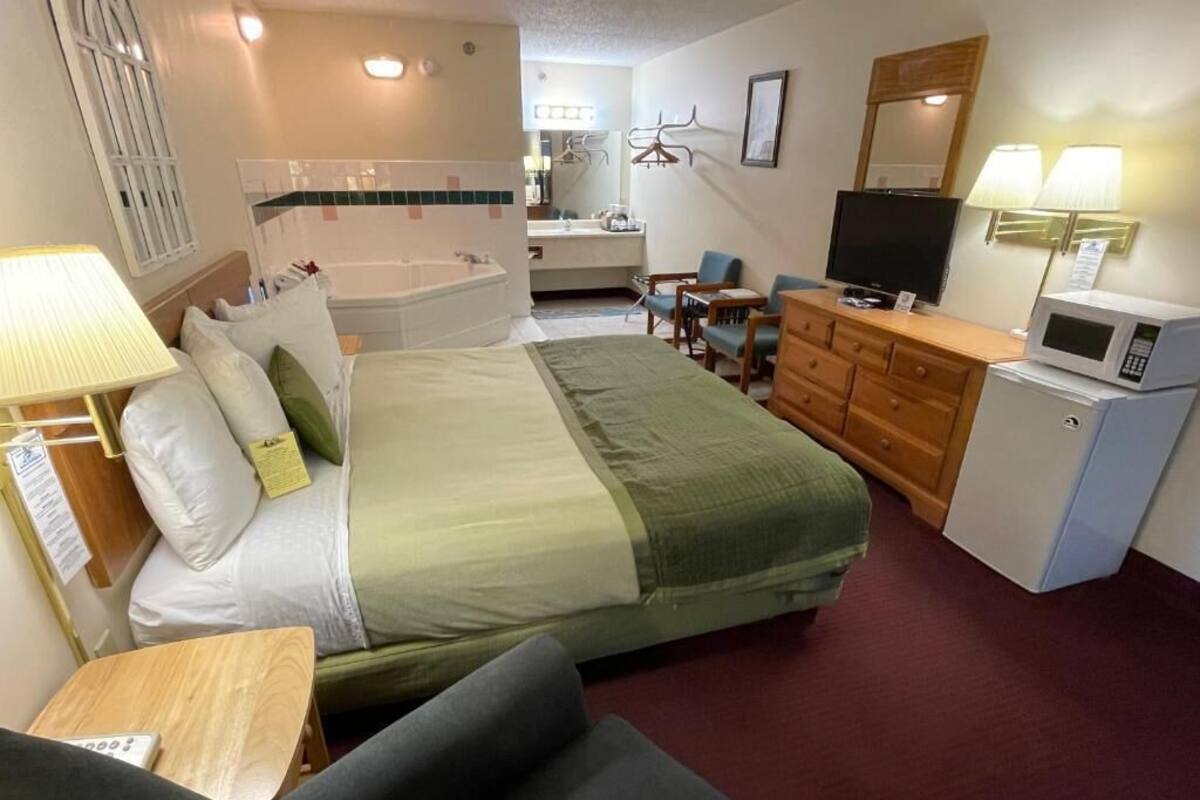 Habitación de hotel con cama, sofá, escritorio, televisor, microondas, cómoda y baño con bañera y ducha.