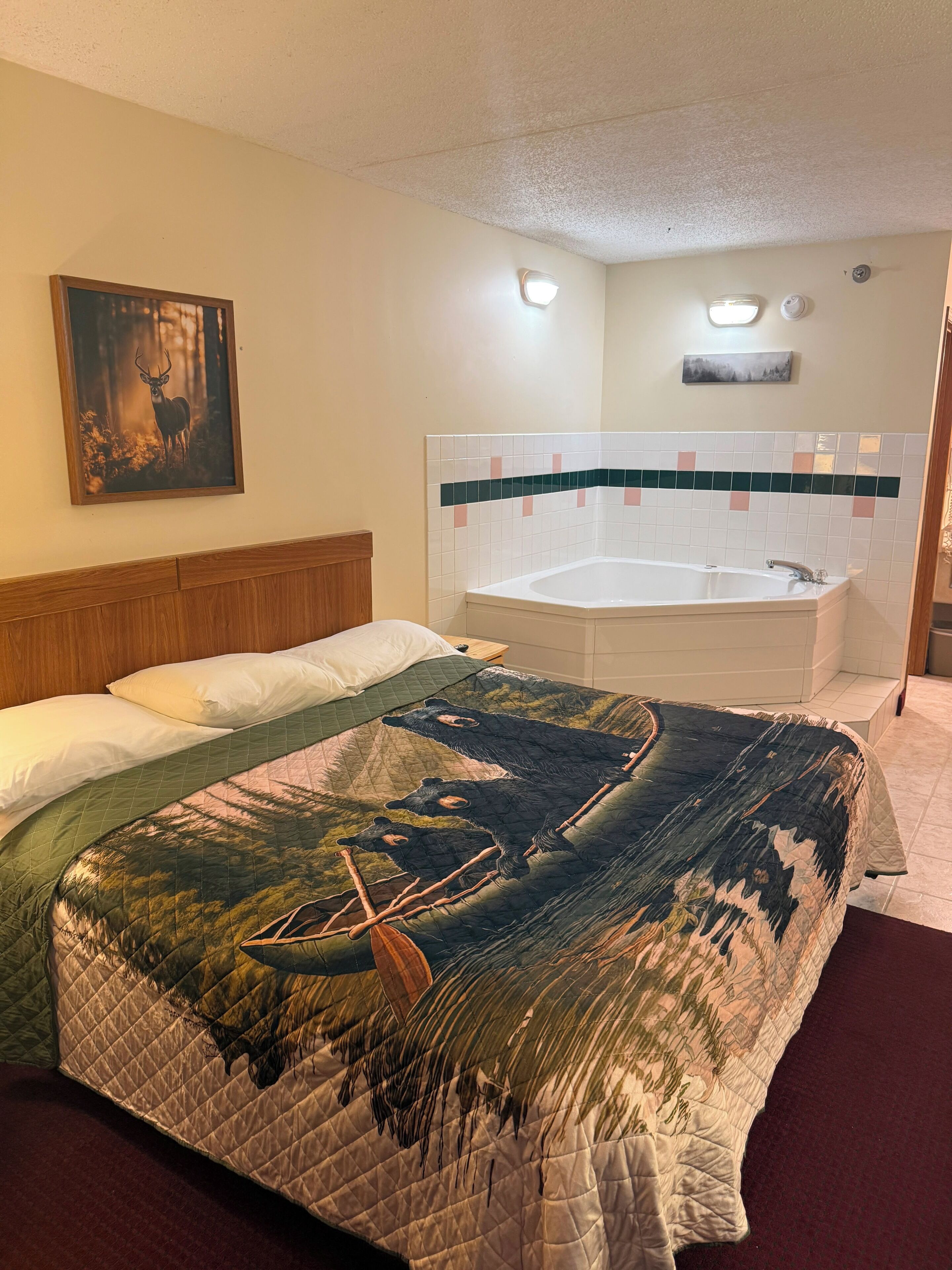 A hotel room with a large bed, a painting of a deer, a bathroom with a bathtub, and a tiled wall.